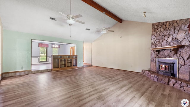 1135 Cook Rd, Texarkana, AR 71854 - unfurnished living room featuring beamed ceiling, wood finished floors, ceiling fan, a wood stove, and a textured ceiling