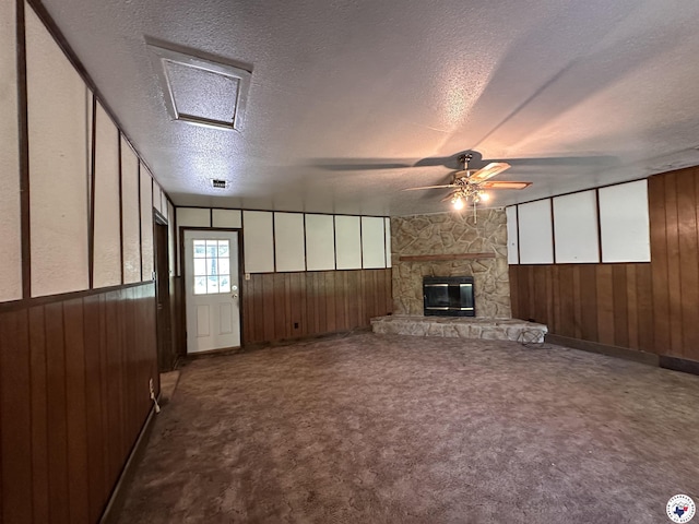 216 W Pioneer St, Wake Village, TX 75501 - unfurnished living room featuring wood walls, a textured ceiling, a ceiling fan, a stone fireplace, and carpet flooring