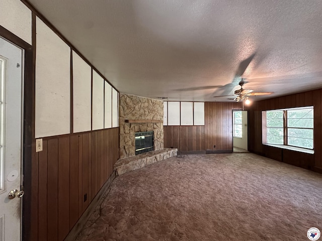 216 W Pioneer St, Wake Village, TX 75501 - unfurnished living room featuring wooden walls, a textured ceiling, carpet floors, a ceiling fan, and a fireplace
