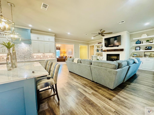 living room with visible vents, light wood-style floors, ornamental molding, and a fireplace