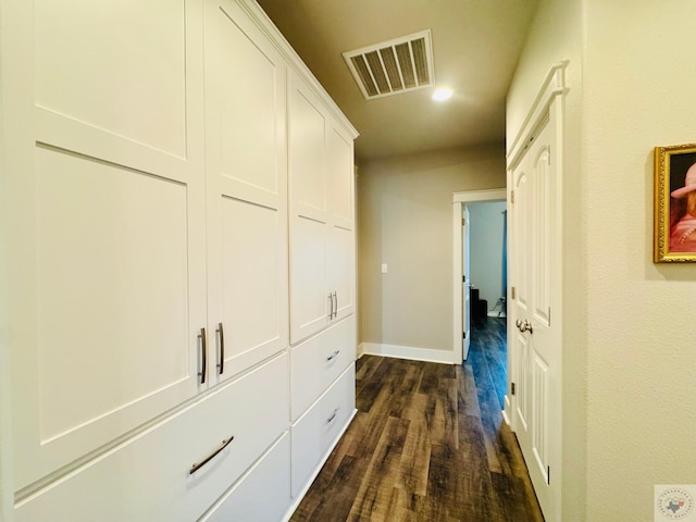 corridor featuring visible vents, baseboards, and dark wood-type flooring