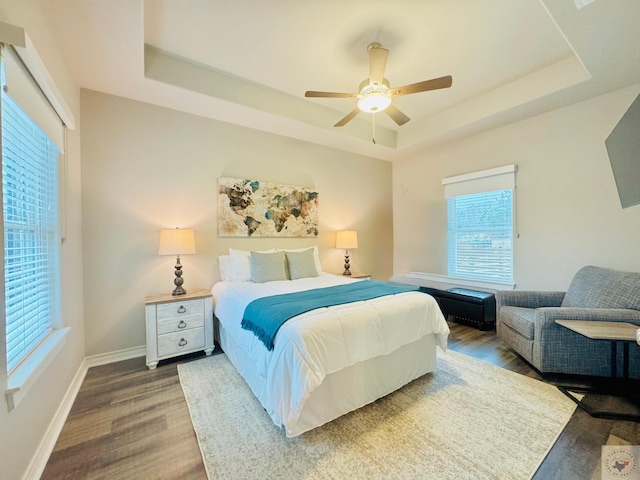 bedroom with ceiling fan, baseboards, a tray ceiling, and wood finished floors