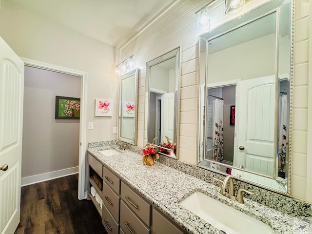 full bath featuring double vanity, wood finished floors, baseboards, and a sink