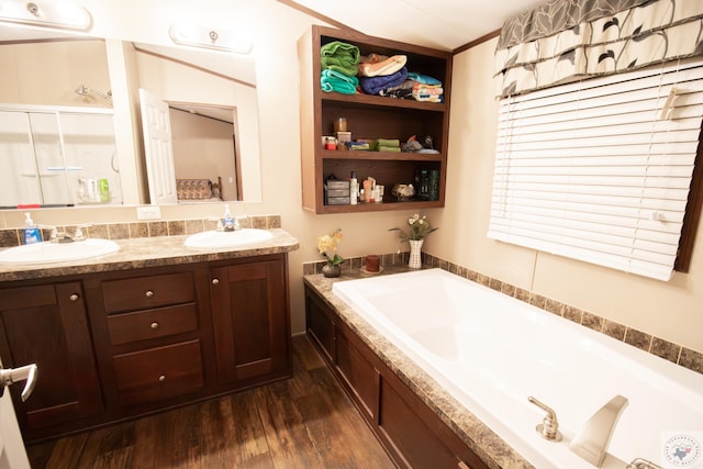 full bathroom with a sink, wood finished floors, double vanity, and a bath