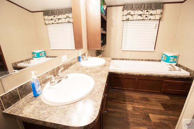 full bath with double vanity, a bath, wood finished floors, and a sink