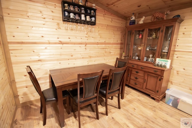 dining room featuring wooden walls, light wood-style flooring, and vaulted ceiling