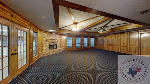 unfurnished living room with a textured ceiling, french doors, vaulted ceiling with beams, a fireplace, and wood walls