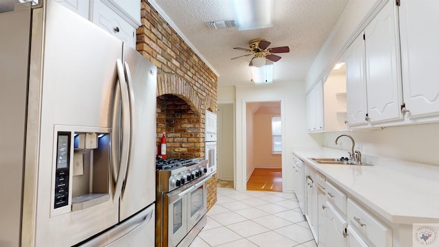 kitchen with appliances with stainless steel finishes, a textured ceiling, white cabinetry, light tile patterned floors, and sink