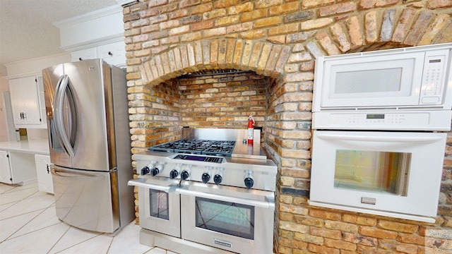 kitchen featuring brick wall, white cabinetry, stainless steel appliances, ornamental molding, and light tile patterned floors