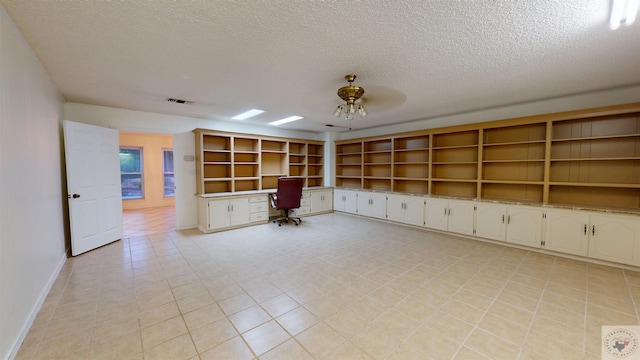 unfurnished office with ceiling fan, built in desk, a textured ceiling, and light tile patterned flooring