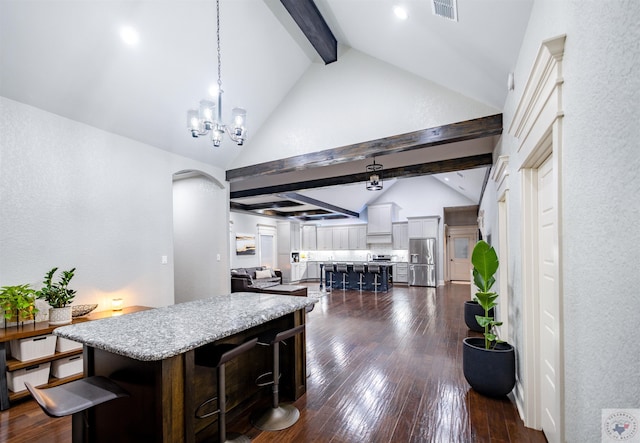 kitchen featuring a center island, stainless steel refrigerator with ice dispenser, decorative light fixtures, a breakfast bar, and lofted ceiling with beams