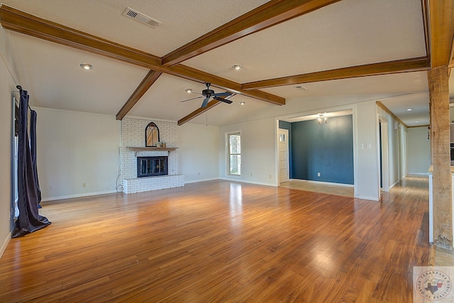 unfurnished living room with hardwood / wood-style floors, a textured ceiling, ceiling fan, lofted ceiling with beams, and a brick fireplace