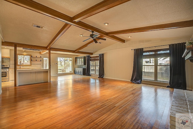 unfurnished living room featuring ceiling fan, a textured ceiling, lofted ceiling with beams, and light wood-type flooring