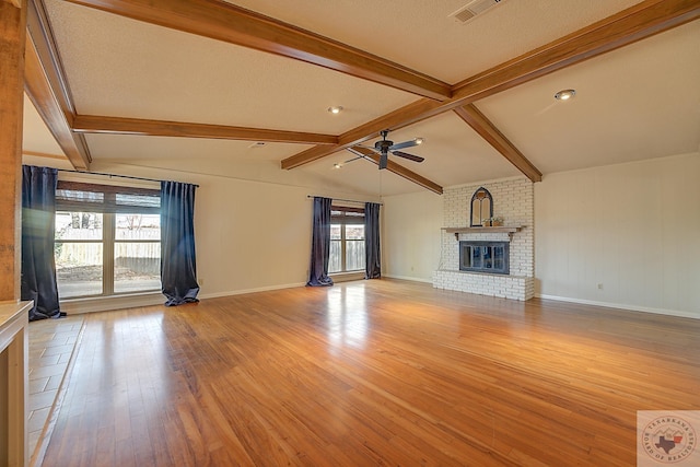 unfurnished living room featuring ceiling fan, a brick fireplace, light hardwood / wood-style flooring, and lofted ceiling with beams