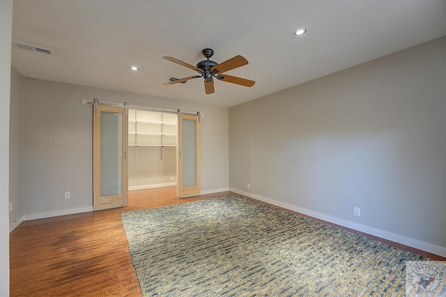 unfurnished room with ceiling fan, hardwood / wood-style floors, and a barn door