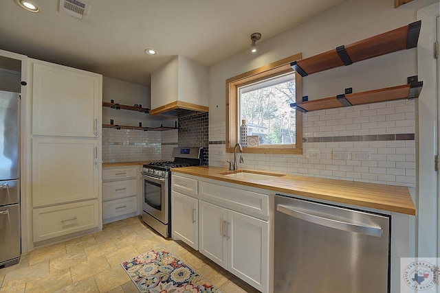 kitchen featuring wooden counters, sink, premium range hood, white cabinetry, and stainless steel appliances