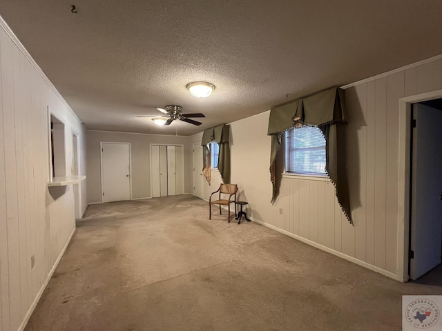 interior space with crown molding, a textured ceiling, wooden walls, light carpet, and ceiling fan