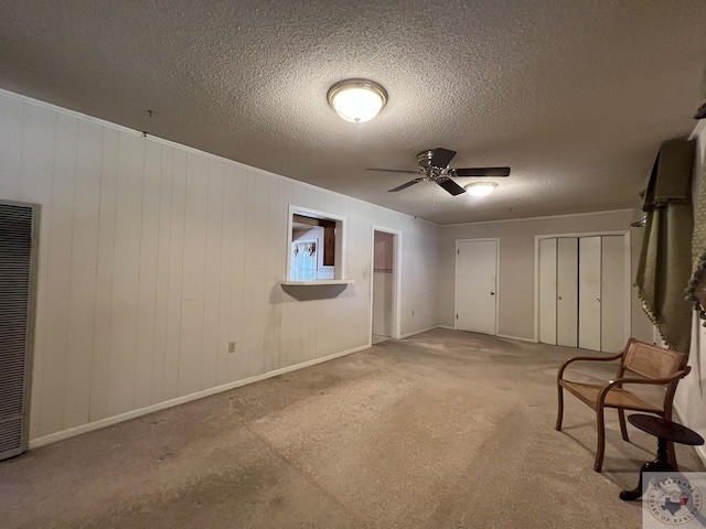 basement featuring ceiling fan, light colored carpet, a textured ceiling, and wooden walls