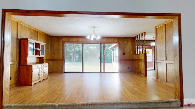 kitchen with wood walls, light hardwood / wood-style floors, a textured ceiling, and hanging light fixtures