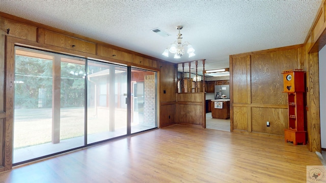 unfurnished living room with a textured ceiling, light wood-type flooring, wooden walls, and a chandelier