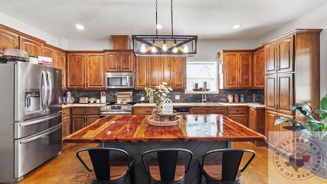 kitchen featuring brown cabinetry, appliances with stainless steel finishes, backsplash, hanging light fixtures, and a sink