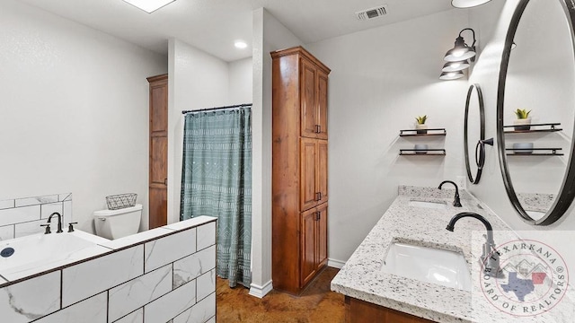 bathroom with toilet, double vanity, visible vents, and a sink