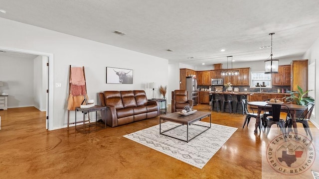 living area featuring finished concrete flooring, visible vents, baseboards, a textured ceiling, and recessed lighting