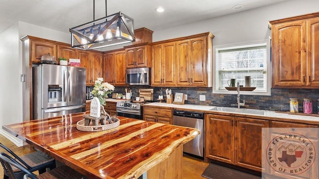 kitchen with pendant lighting, stainless steel appliances, backsplash, brown cabinetry, and a sink