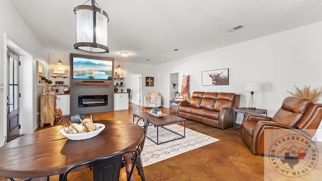 living room with finished concrete flooring, a glass covered fireplace, and visible vents