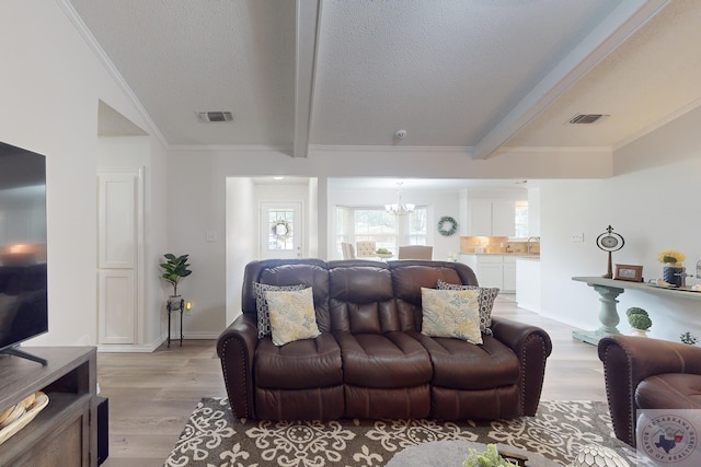 living room with a textured ceiling, beamed ceiling, an inviting chandelier, light hardwood / wood-style floors, and crown molding