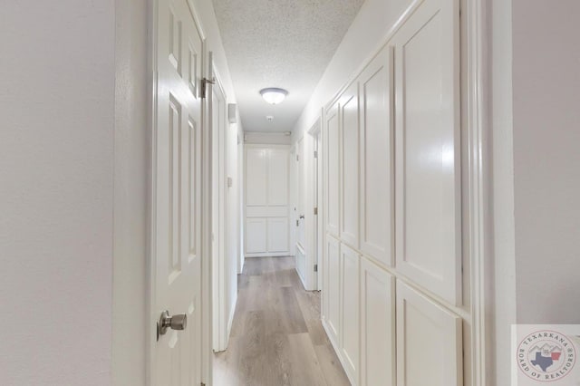 hall with a textured ceiling and light hardwood / wood-style flooring