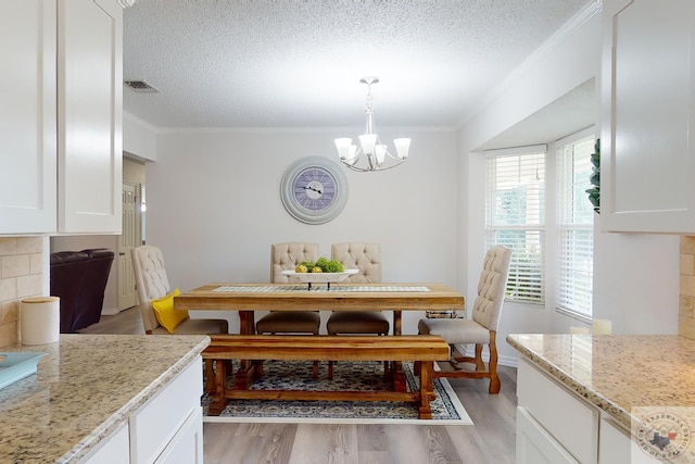 dining area featuring light wood-type flooring, crown molding, an inviting chandelier, and a textured ceiling