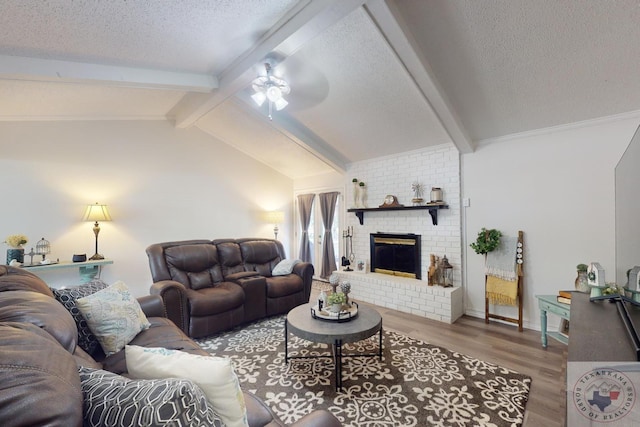 living room with ceiling fan, a fireplace, hardwood / wood-style floors, a textured ceiling, and vaulted ceiling with beams