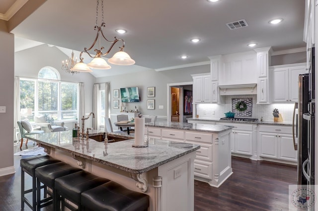 kitchen featuring backsplash, white cabinetry, lofted ceiling, and an island with sink