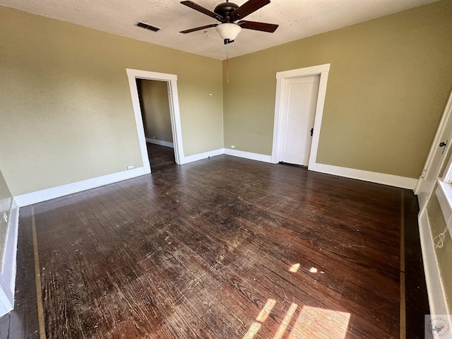 empty room featuring ceiling fan, dark wood-type flooring, and a textured ceiling