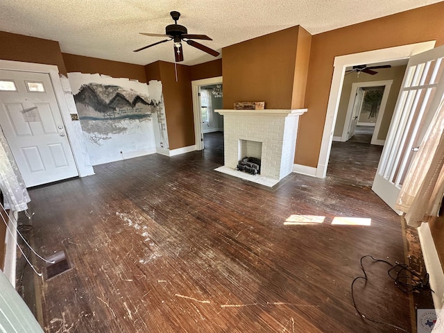 unfurnished living room with ceiling fan, a textured ceiling, dark hardwood / wood-style floors, and a brick fireplace