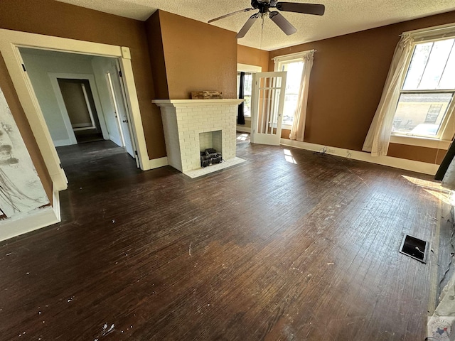 unfurnished living room featuring a brick fireplace, a textured ceiling, dark hardwood / wood-style floors, and ceiling fan