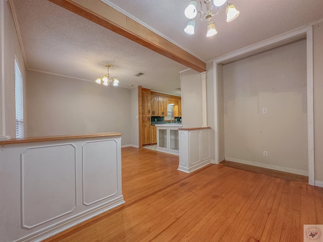 unfurnished living room with crown molding, ornate columns, light wood-type flooring, a textured ceiling, and a notable chandelier