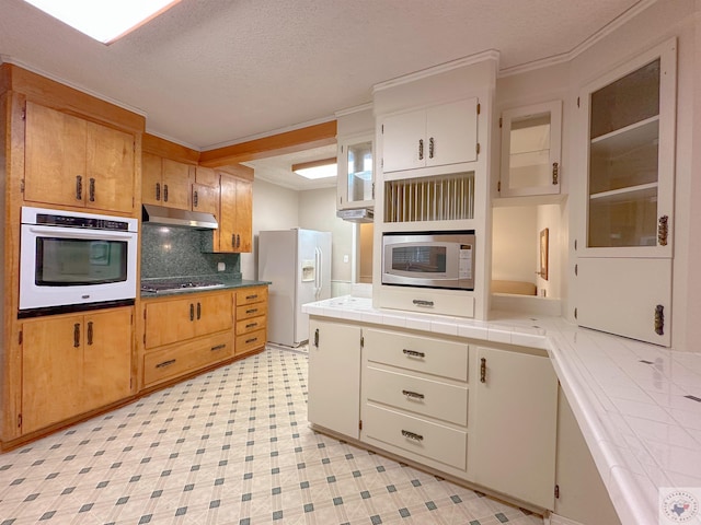 kitchen featuring a textured ceiling, stainless steel appliances, backsplash, tile countertops, and crown molding