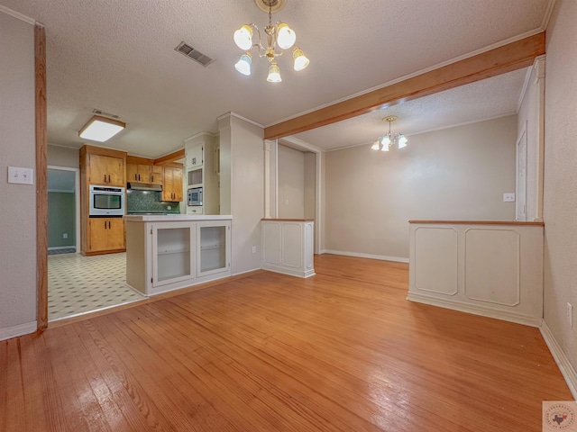 unfurnished living room featuring a chandelier, light hardwood / wood-style floors, and a textured ceiling