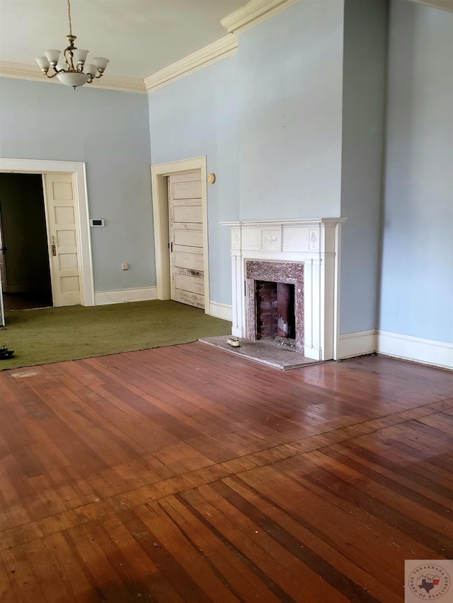 unfurnished living room with dark wood-type flooring, a high end fireplace, crown molding, and an inviting chandelier