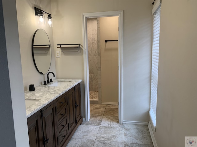 bathroom featuring a sink, baseboards, double vanity, and a tile shower