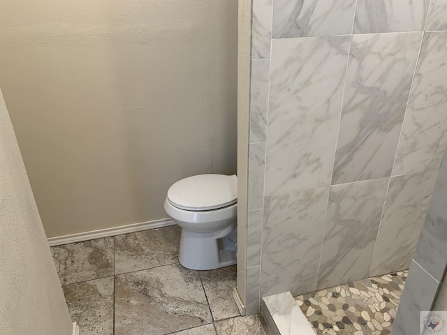 bathroom with toilet, tiled shower, and baseboards