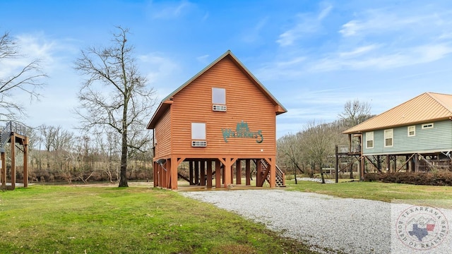 back of property featuring gravel driveway, faux log siding, a carport, and a yard