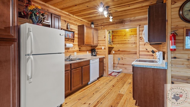 kitchen with white appliances, light countertops, a sink, and wood walls