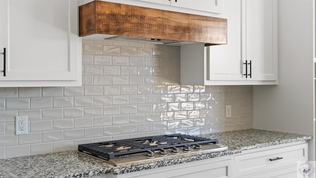 kitchen with stainless steel gas stovetop, custom range hood, backsplash, white cabinetry, and light stone counters