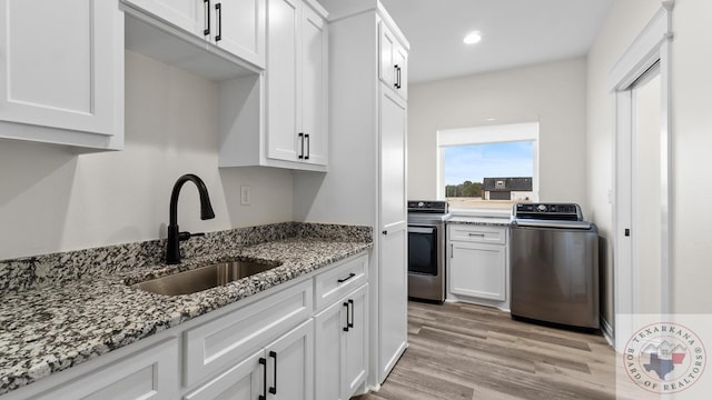 kitchen with light stone countertops, washer / clothes dryer, white cabinetry, sink, and electric stove