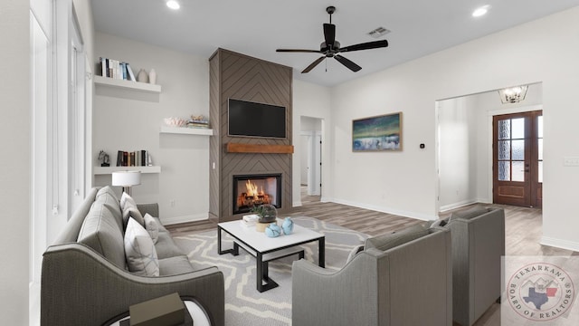 living room with light hardwood / wood-style floors, a large fireplace, and ceiling fan