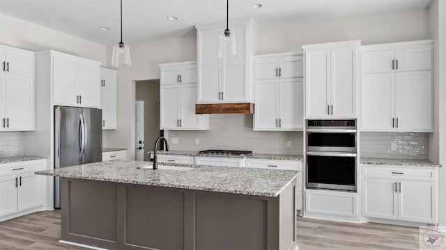 kitchen with appliances with stainless steel finishes, a kitchen island with sink, sink, decorative light fixtures, and white cabinets