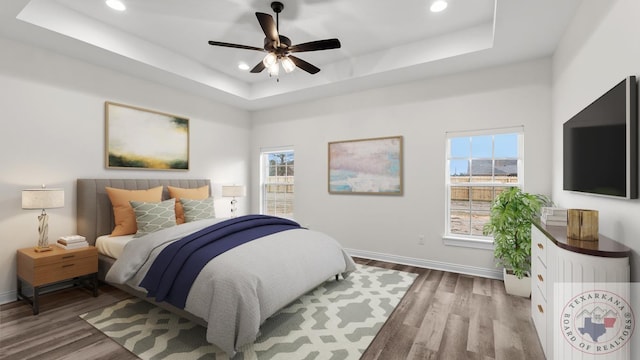 bedroom featuring wood-type flooring, multiple windows, ceiling fan, and a raised ceiling